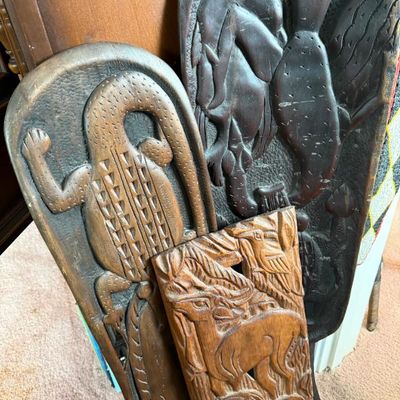 Sale Photo Thumbnail #233: Group of vintage hand-carved African wooden wall plaques and panels, depicting stylized figures, reptiles, and wildlife.