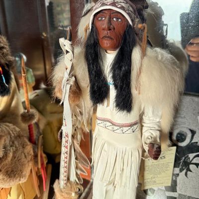 Sale Photo Thumbnail #200: Handcrafted Native American chief doll wearing a detailed feather warbonnet, fringe buckskin outfit, and fur trim, holding a decorative spear.