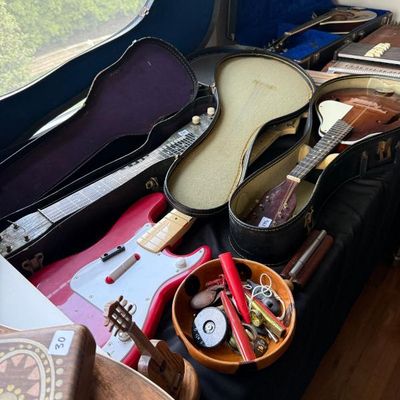Sale Photo Thumbnail #183: Collection of vintage stringed instruments and accessories, including a mandolin in its case, a lap steel guitar, a red toy electric guitar, and a wooden bowl filled with small musical accessories.