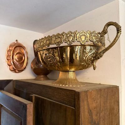 Sale Photo Thumbnail #301: Ornate polished brass footed centerpiece bowl featuring embossed scrolling details, a pierced gallery rim, and ornate handles, displayed alongside a copper gelatin mold and copper pitcher.