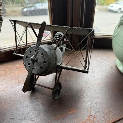 Sale Photo Thumbnail #296: Vintage welded metal biplane sculpture featuring a pilot figure with goggles, sitting on a wooden windowsill.
