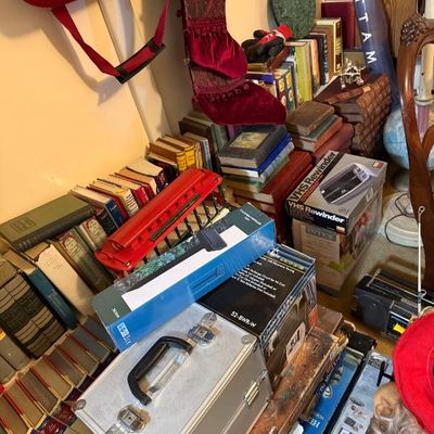 Sale Photo Thumbnail #159: A collection of household goods and media, including vintage books, boxed electronics, a VHS rewinder, a small aluminum briefcase, and holiday decor.
