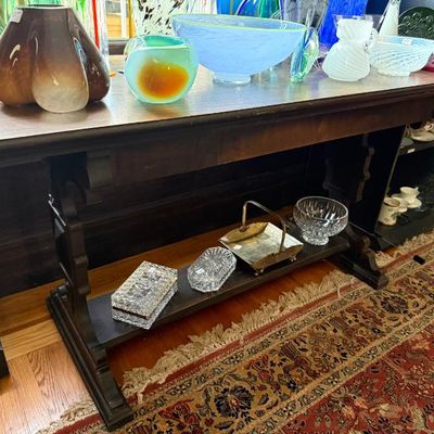 Sale Photo Thumbnail #254: Dark wood trestle sofa table with a lower shelf, topped with an assortment of colorful art glass bowls and vases.