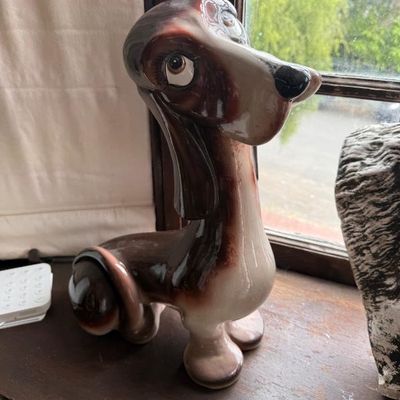 Sale Photo Thumbnail #294: Vintage stylized ceramic dachshund figurine featuring a high-gloss brown and cream glaze with exaggerated, expressive facial features.