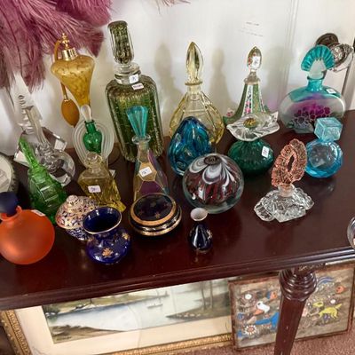 Sale Photo Thumbnail #274: Collection of vintage and antique glass perfume bottles, atomizers, and art glass paperweights displayed on a wooden console table.