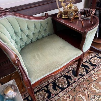Sale Photo Thumbnail #299: Vintage wood telephone gossip bench with button-tufted light green velvet upholstery, featuring a brass French-style rotary phone on the side table.