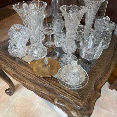 Sale Photo Thumbnail #316: Collection of vintage cut glass and crystal tableware, including tall vases, stemware, small bowls, and covered dishes, displayed on a wooden end table.