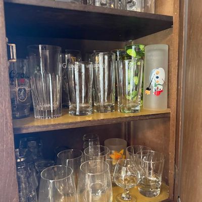 Sale Photo Thumbnail #370: Wooden cabinet shelves filled with assortment of vintage drinking glasses, branded beer pint glasses, stein mugs, and novelty glassware.