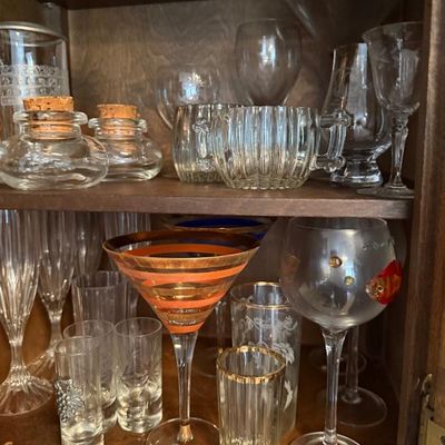 Sale Photo Thumbnail #308: Collection of vintage glassware on wooden cabinet shelves, including copper-striped martini glasses, corked inkwells, and etched stemware.