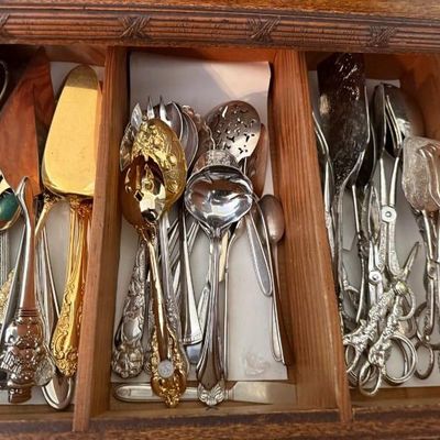 Sale Photo Thumbnail #322: Collection of vintage silver-plated and brass serving utensils, including pie servers, slotted spoons, tongs, and ladles, displayed in a wooden organizer shelf.