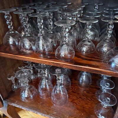 Sale Photo Thumbnail #319: Large collection of vintage etched crystal glassware stored upside down on wood cabinet shelves, featuring ball-stem designs and floral cut motifs.