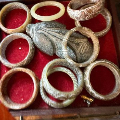 Sale Photo Thumbnail #42: Collection of carved jade and hardstone bangles alongside a carved stone cicada object, displayed in a red velvet-lined tray.
