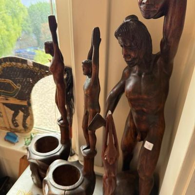 Sale Photo Thumbnail #230: Collection of hand-carved dark wood tribal figures and sculptural vessels, featuring standing human forms with raised arms.