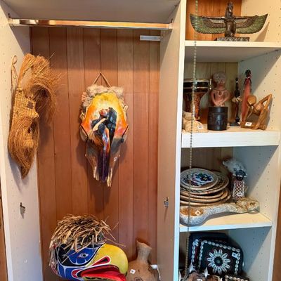 Sale Photo Thumbnail #205: Collection of global ethnographic and Indigenous art objects, including a hand-painted skull hanging, a Pacific Northwest style raven mask on a stand, woven decor, carved wooden sculptures, and beaded items.