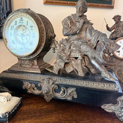 Sale Photo Thumbnail #360: Antique French or Victorian figural mantel clock featuring a seated scholar sculpture mounted on a dark stone base with ornate metal trim.