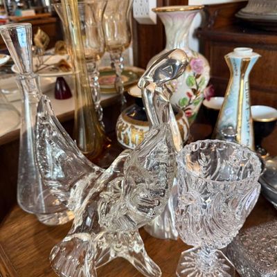 Sale Photo Thumbnail #327: Collection of vintage glass and porcelain items, including a clear glass eagle figurine, cut crystal goblet, amber stretch vase, and floral ceramic vases.