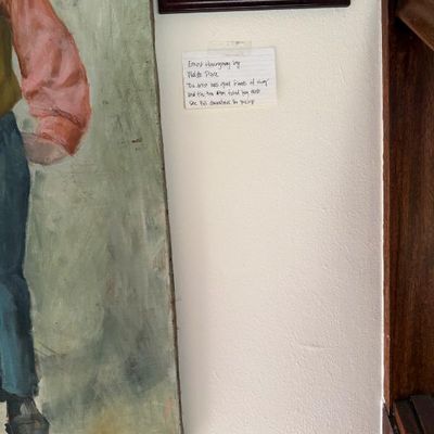 Sale Photo Thumbnail #45: Oil painting depicting Ernest Hemingway by Waldo Peirce, displayed on a wall with accompanying provenance note.