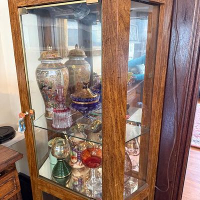 Sale Photo Thumbnail #324: Tall wood display cabinet with glass front and side panels, housing an assortment of decorative glassware and porcelain urns.