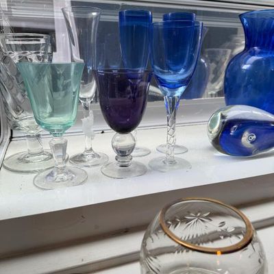 Sale Photo Thumbnail #372: Collection of assorted glassware, including cobalt blue stemware, a light green goblet, purple wine glass, clear champagne flute, and a gold-rimmed cut glass bowl.