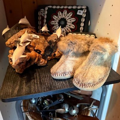 Sale Photo Thumbnail #201: Collection of decorative items including fur-lined boots, a driftwood sculpture with carved white dolphins, and a shell-embellished textile artwork.