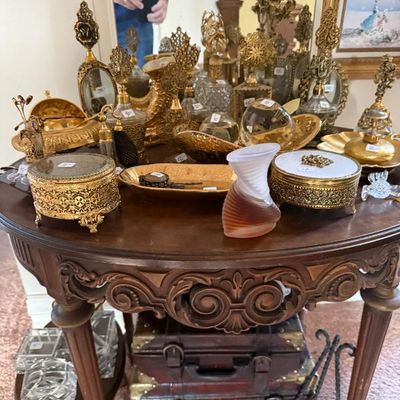 Sale Photo Thumbnail #256: Collection of ornate vintage filigree perfume bottles and vanity trinket boxes displayed on a carved wooden side table.
