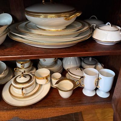 Sale Photo Thumbnail #13: Collection of white porcelain dinnerware and serveware with ornate gold trim, including a covered tureen, platters, teacups, and creamer, stored inside a wooden cabinet.