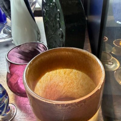 Sale Photo Thumbnail #330: Collection of decorative glassware and ceramics, featuring a two-tone speckled cylindrical vase, a purple art glass vessel, and a dark green embossed flask vase.