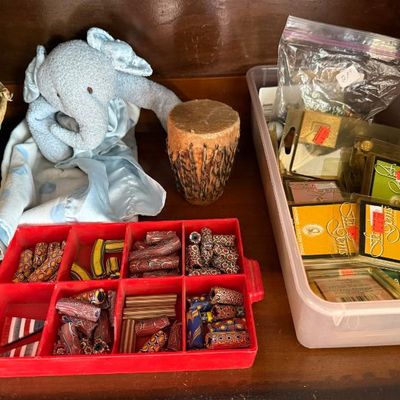 Sale Photo Thumbnail #259: Collection of assorted craft items including colorful trade beads in a red organizer tray, packaged Star Gems, a miniature drum, a plush elephant lovey, and a small woven basket.