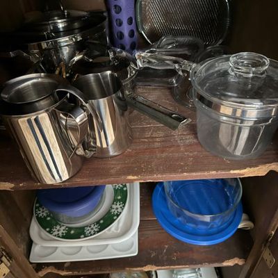 Sale Photo Thumbnail #363: Assorted vintage and modern kitchenware stored on wooden cabinet shelves, including stainless steel pitchers, glass cookware, a water bottle, and ceramic serving pieces.