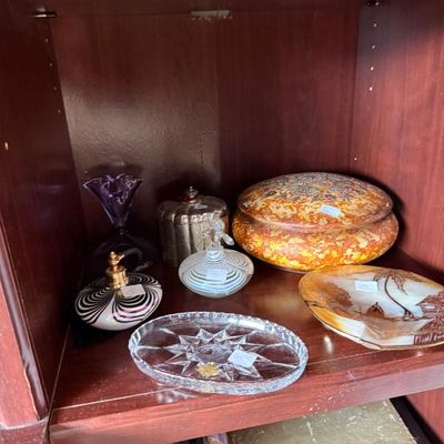 Sale Photo Thumbnail #241: Collection of vintage glass and ceramic decorative items arranged on a shelf, including art glass perfume bottles, a cut crystal tray, and a mottled ceramic covered bowl.