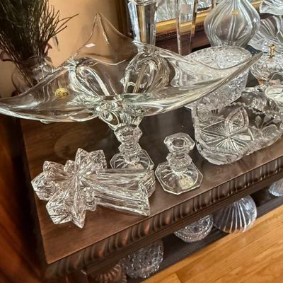 Sale Photo Thumbnail #344: Collection of clear crystal glassware including a large freeform footed bowl, candlesticks, cut crystal dishes, and a decanter arranged on a wooden table.