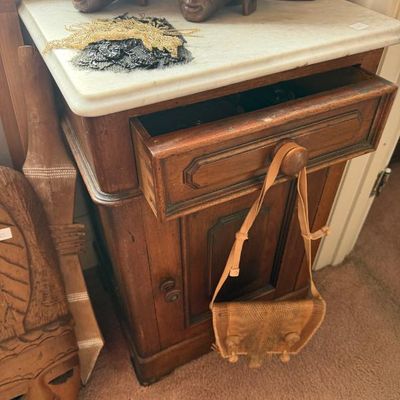 Sale Photo Thumbnail #252: Antique wooden marble-top nightstand with single drawer and lower cabinet, holding carved wooden heads and jewelry, flanked by tribal masks.