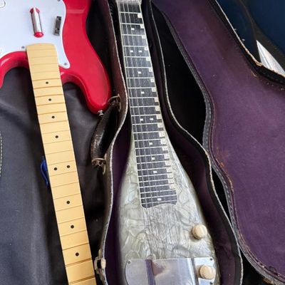 Sale Photo Thumbnail #181: Vintage pearloid lap steel guitar with original hard case, displayed next to a red electric guitar body and maple neck.