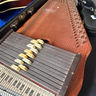 Sale Photo Thumbnail #178: Vintage Oscar Schmidt autoharp with a wooden soundboard and cream-colored chord bars, displayed alongside musical instrument cases.