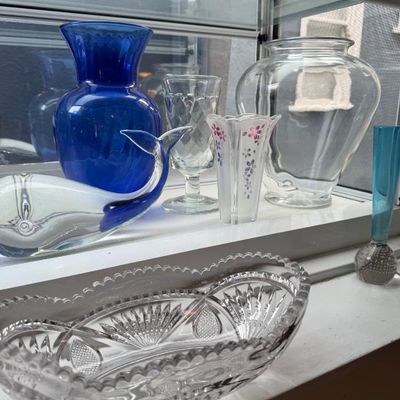 Sale Photo Thumbnail #371: Collection of decorative glassware displayed on a window sill, including a cobalt blue vase, a clear art glass whale figurine, a cut glass serving dish, and various small vases.