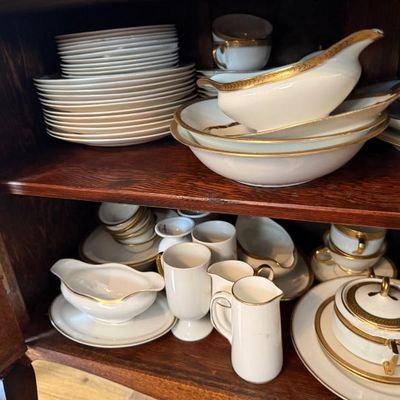 Sale Photo Thumbnail #12: Collection of white and gold porcelain dinnerware, including plates, bowls, creamers, sugar bowls, and gravy boats, arranged inside a wooden cabinet.