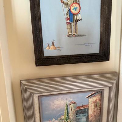Sale Photo Thumbnail #195: Two framed wall art pieces, including a top painting of a Native American chief signed by Dave Paulley and a lower framed oil painting depicting a European coastal village scene.