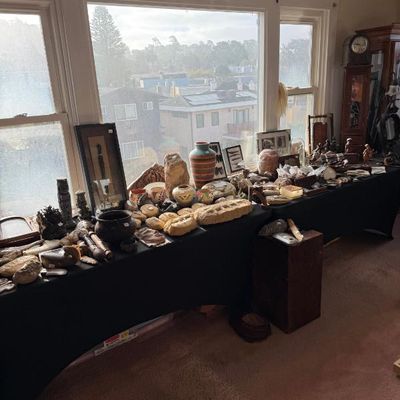 Sale Photo Thumbnail #197: Collection of Southwestern pottery, fossils, stones, framed art, and decorative artifacts arranged on a long, black cloth-covered display table in front of a window.