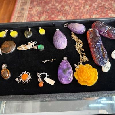 Sale Photo Thumbnail #33: Jewelry display tray containing an assortment of stone and resin pendants, including charoite tear drops, carved amber-colored pieces, and silver-tone mounted cabs.