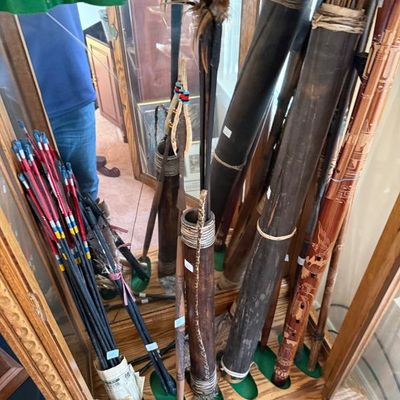 Sale Photo Thumbnail #209: Collection of indigenous-style wooden quivers, arrows, carved flutes, and spears stored in a mirrored wooden display cabinet.