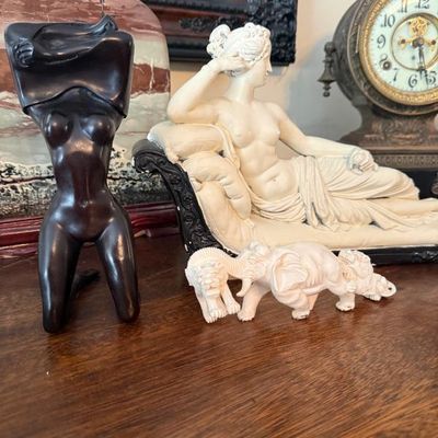 Sale Photo Thumbnail #30: Collection of decorative sculptures including a dark wood abstract female torso, a reclining Classical resin figure on a lounge, and a carved elephant procession figurine.