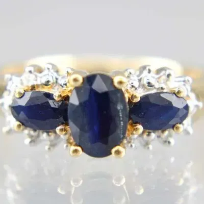 Two-tone gold ring featuring three oval-cut dark blue sapphires surrounded by diamond-cut beaded accents.