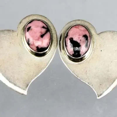 Pair of sterling silver asymmetric heart-shaped earrings featuring bezel-set oval rhodonite cabochons.