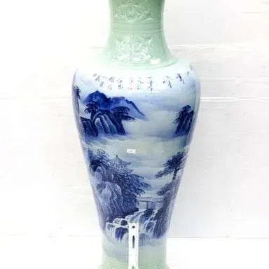 Large Chinese porcelain vase featuring a blue and white landscape scene flanked by pale celadon relief-carved neck and base sections.