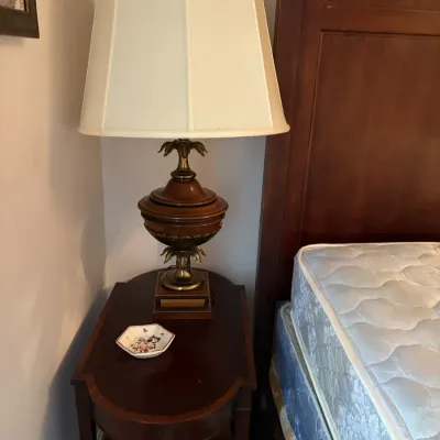 Sale Photo Thumbnail #121: Traditional wooden urn-style table lamp with brass acanthus leaves and a pleated fabric shade, set on a dark wood nightstand.
