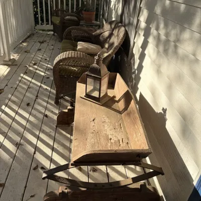 Sale Photo Thumbnail #109: Rustic wooden cradle bench with leaf spring rockers on a porch alongside woven wicker outdoor seating.