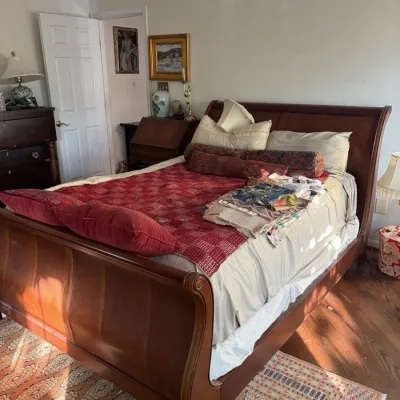 Sale Photo Thumbnail #56: Traditional wooden sleigh bed with bedding and decorative pillows, set in a bedroom with a matching wooden dresser and slant-front desk in the background.