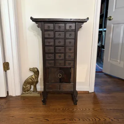 Sale Photo Thumbnail #55: Asian-style dark wood apothecary cabinet with small drawers and lower cabinet, alongside a brass dog doorstop.