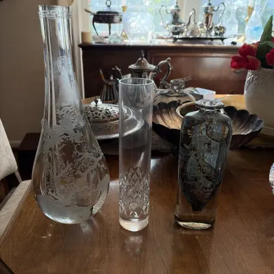 Sale Photo Thumbnail #123: Trio of decorative glass vases, including a large teardrop-shaped vase with etched landscape details, a cut-crystal cylinder vase, and a heavy artistic smoked-glass bottle.