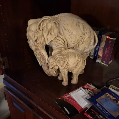 Sale Photo Thumbnail #51: Faux-ivory molded resin figurine of an elephant and calf with textured detailing, resting inside a dark wood cabinet.